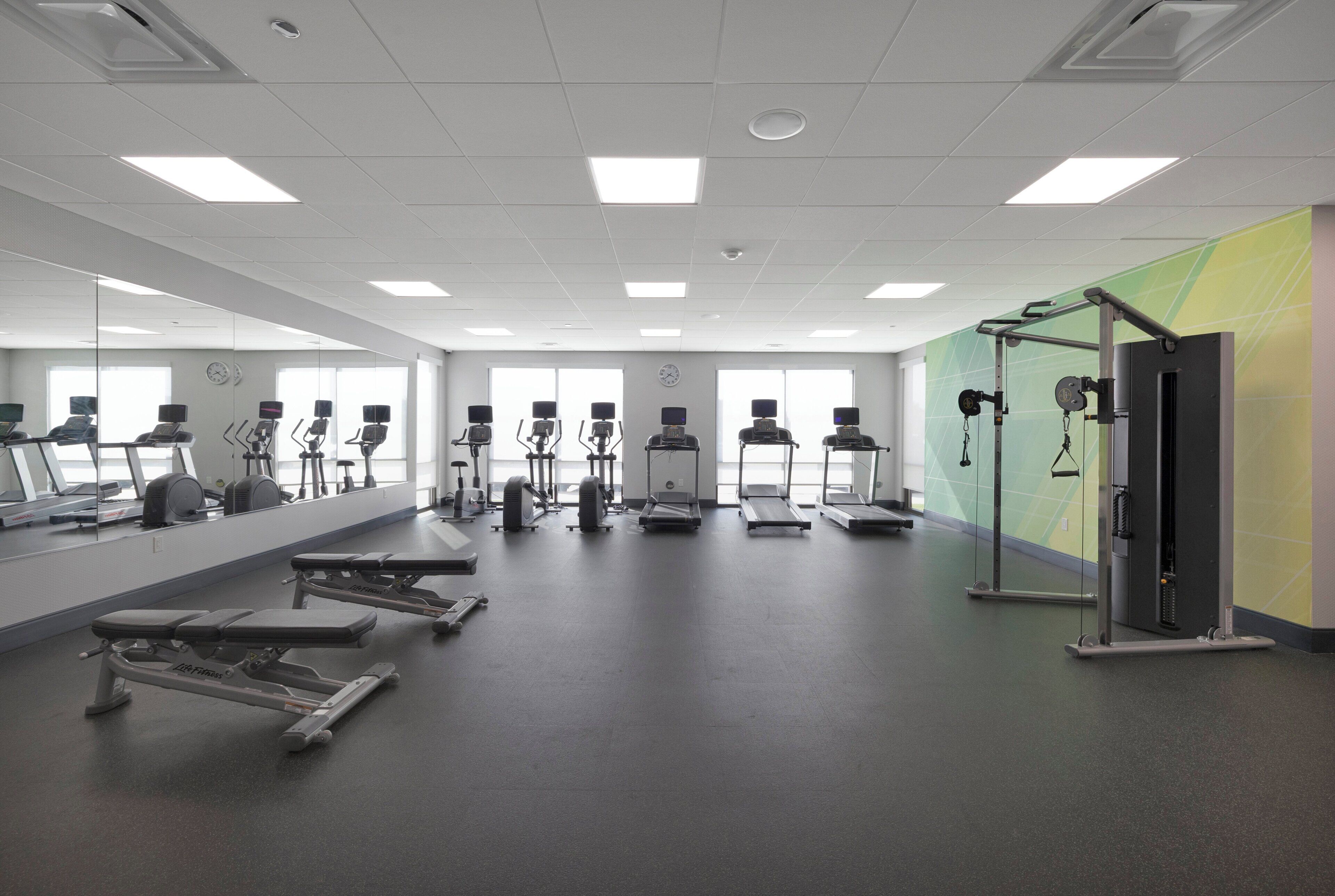 A gym with exercise equipment, mirrors, and a large window.