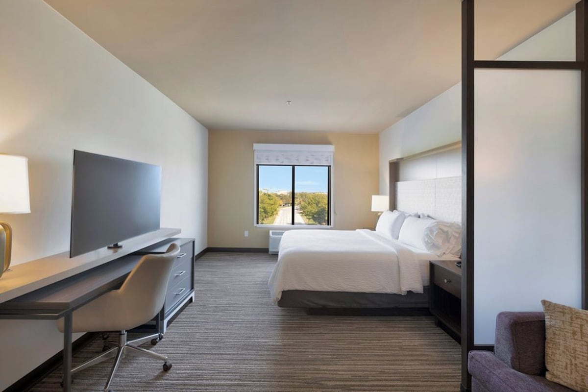 Een hotelkamer met een bed, een bureau met stoel, een televisie en een raam met uitzicht.