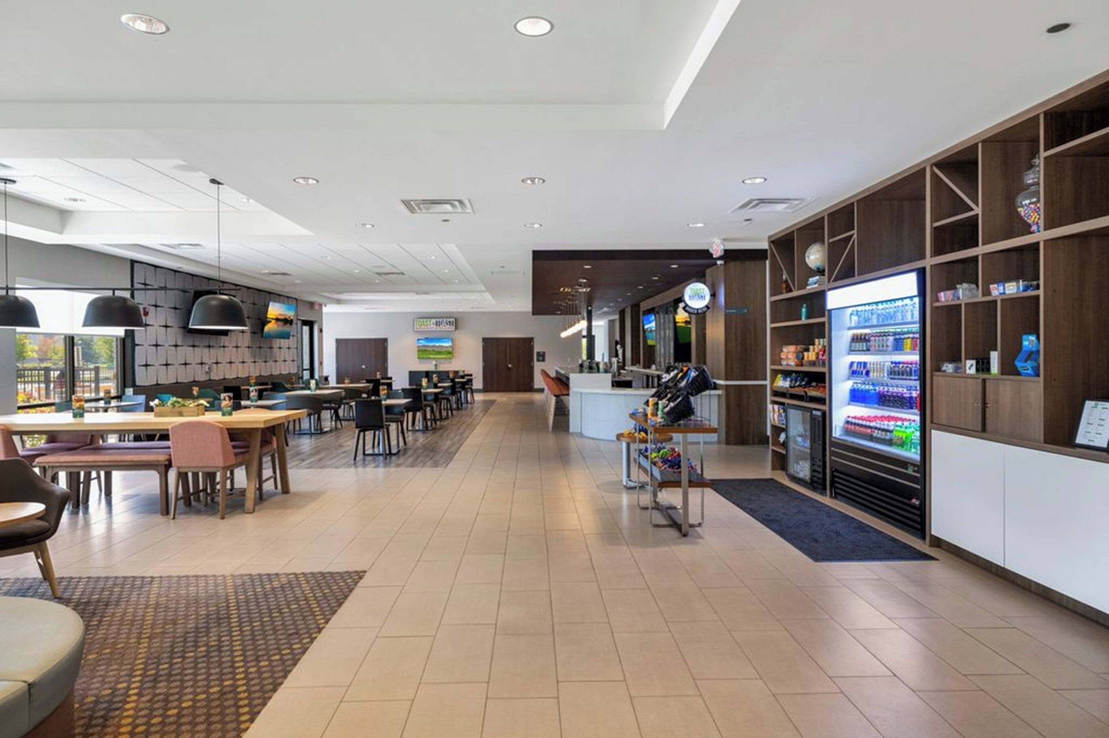 A modern hotel lobby with a reception desk, a vending machine, and a seating area with tables and chairs.