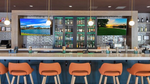 A bar area with a long counter, multiple bar stools, and two large TVs displaying scenic images.