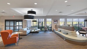 A spacious lobby with a modern design, featuring a large seating area with sofas and armchairs, a coffee table, and a patterned carpet.