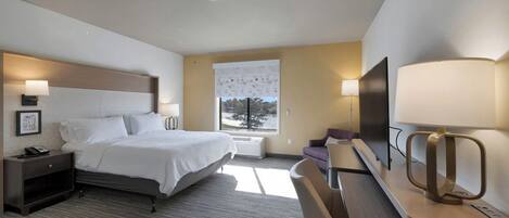 A hotel room with a bed, bedside table, lamp, TV, and a desk with a chair.