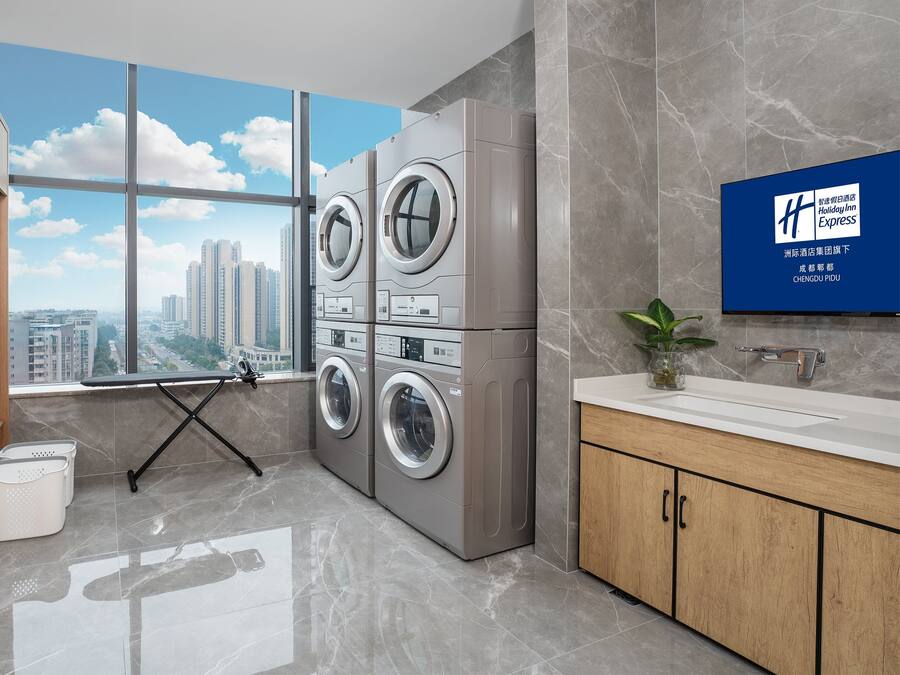 A modern hotel room with a large window, a washing machine, a drying rack, and a sink with a mirror.