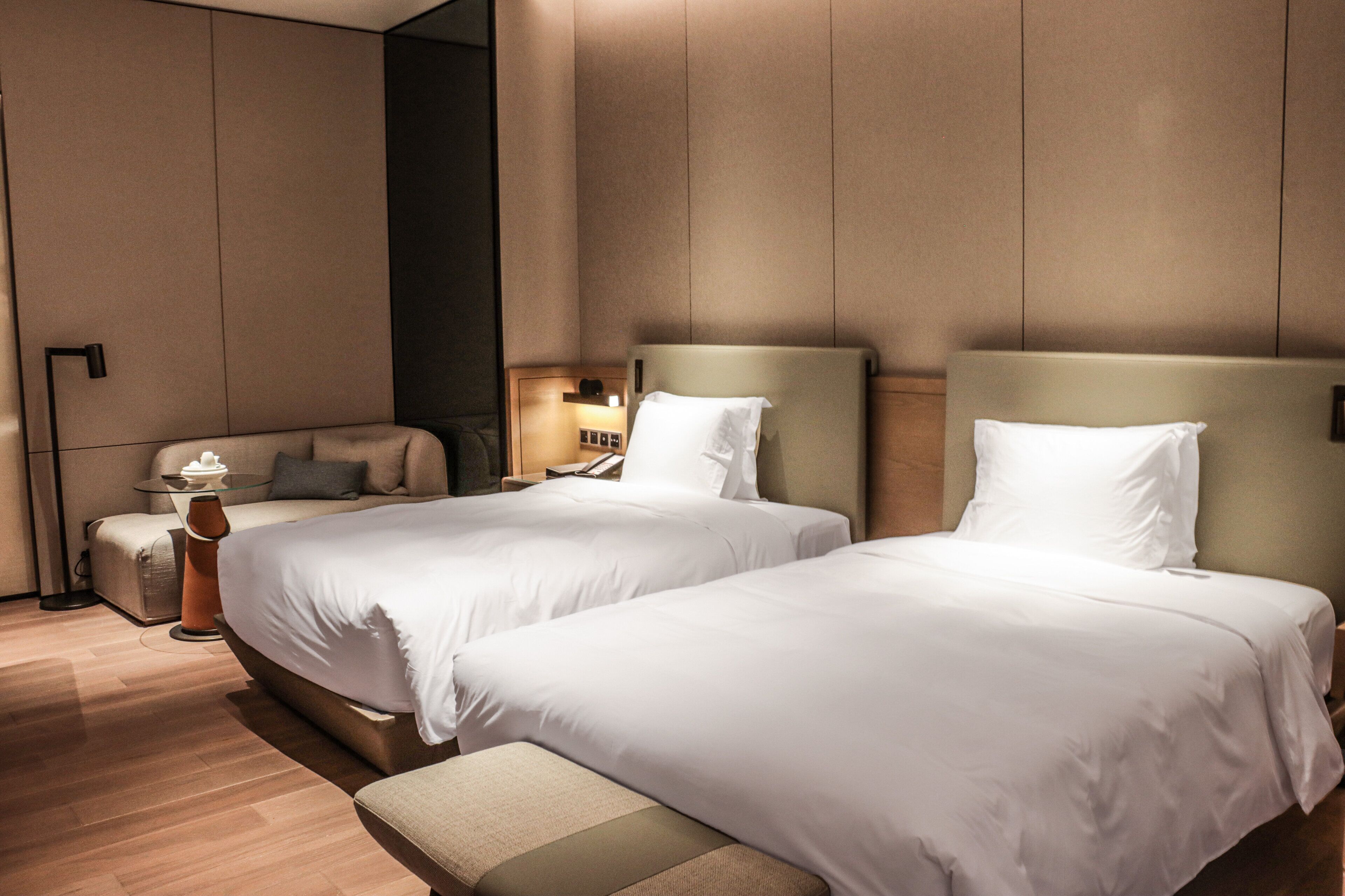 Habitación de hotel con dos camas, una mesita de noche, una lámpara y un banco.
