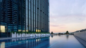 Un hôtel moderne doté d’une piscine à débordement sur le toit, d’un immeuble de grande hauteur avec des balcons et d’un ciel dégagé.