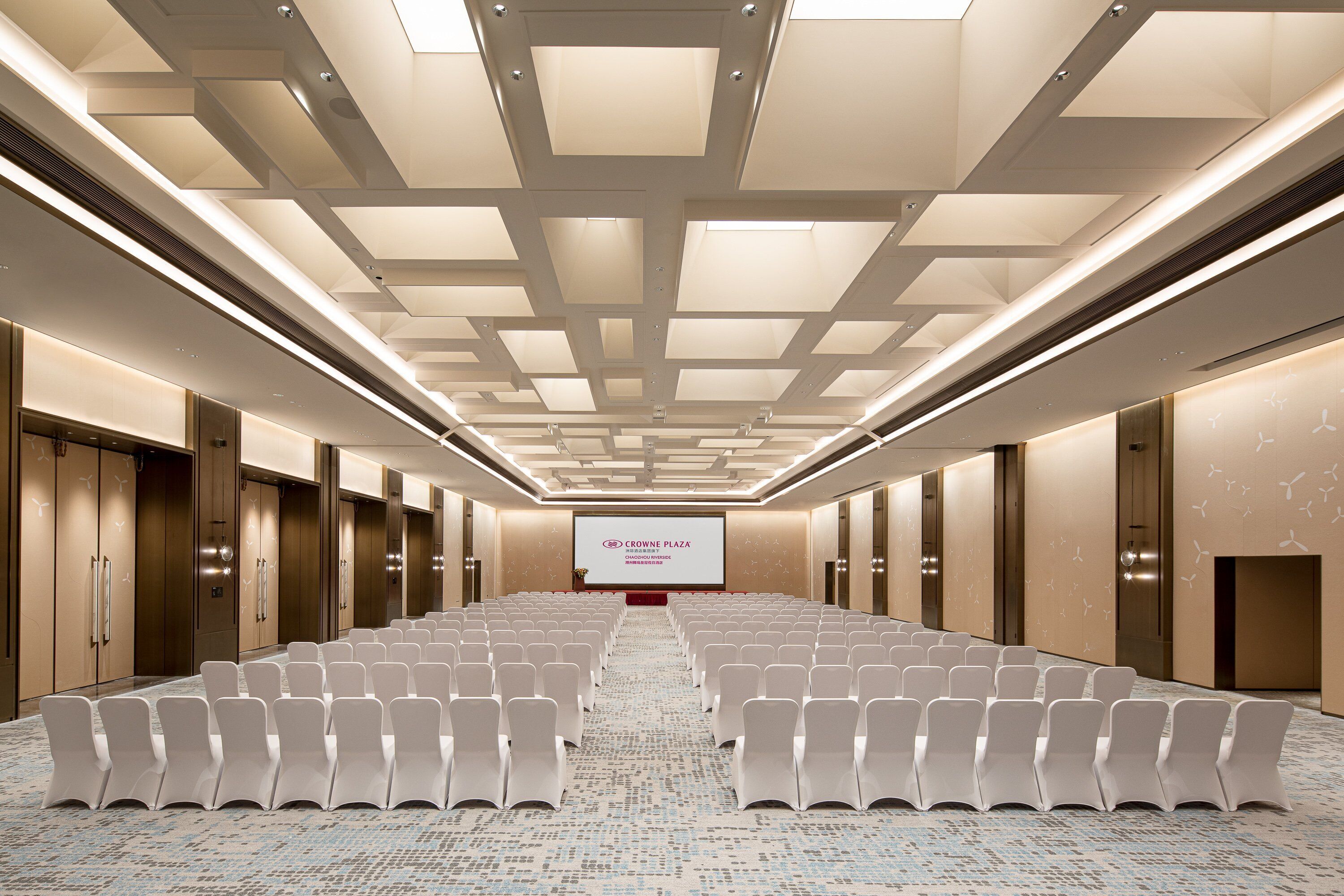 A conference room with rows of chairs, a projector screen, and a patterned carpet.