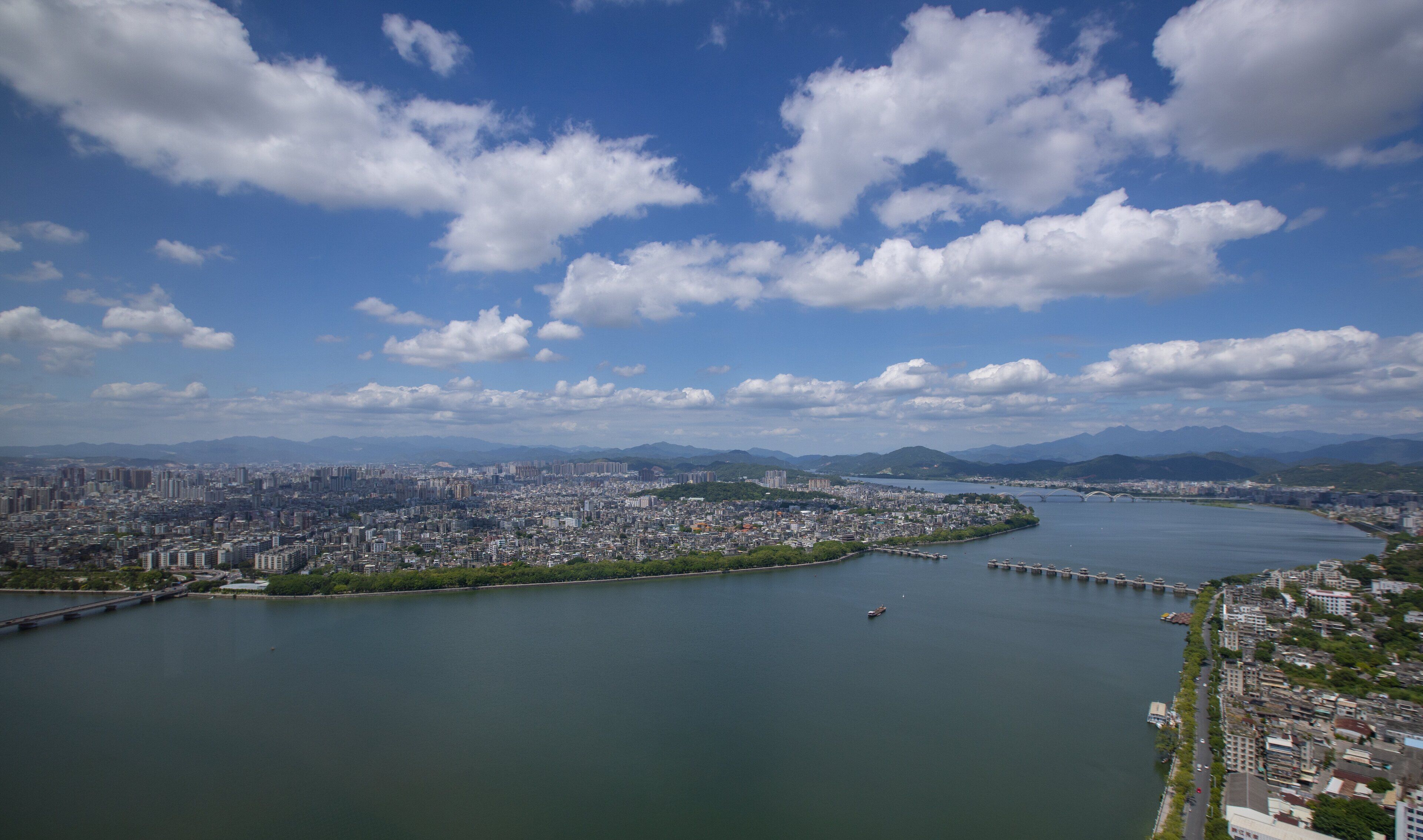 Vista panorámica de una ciudad con un río, puentes y montañas al fondo.