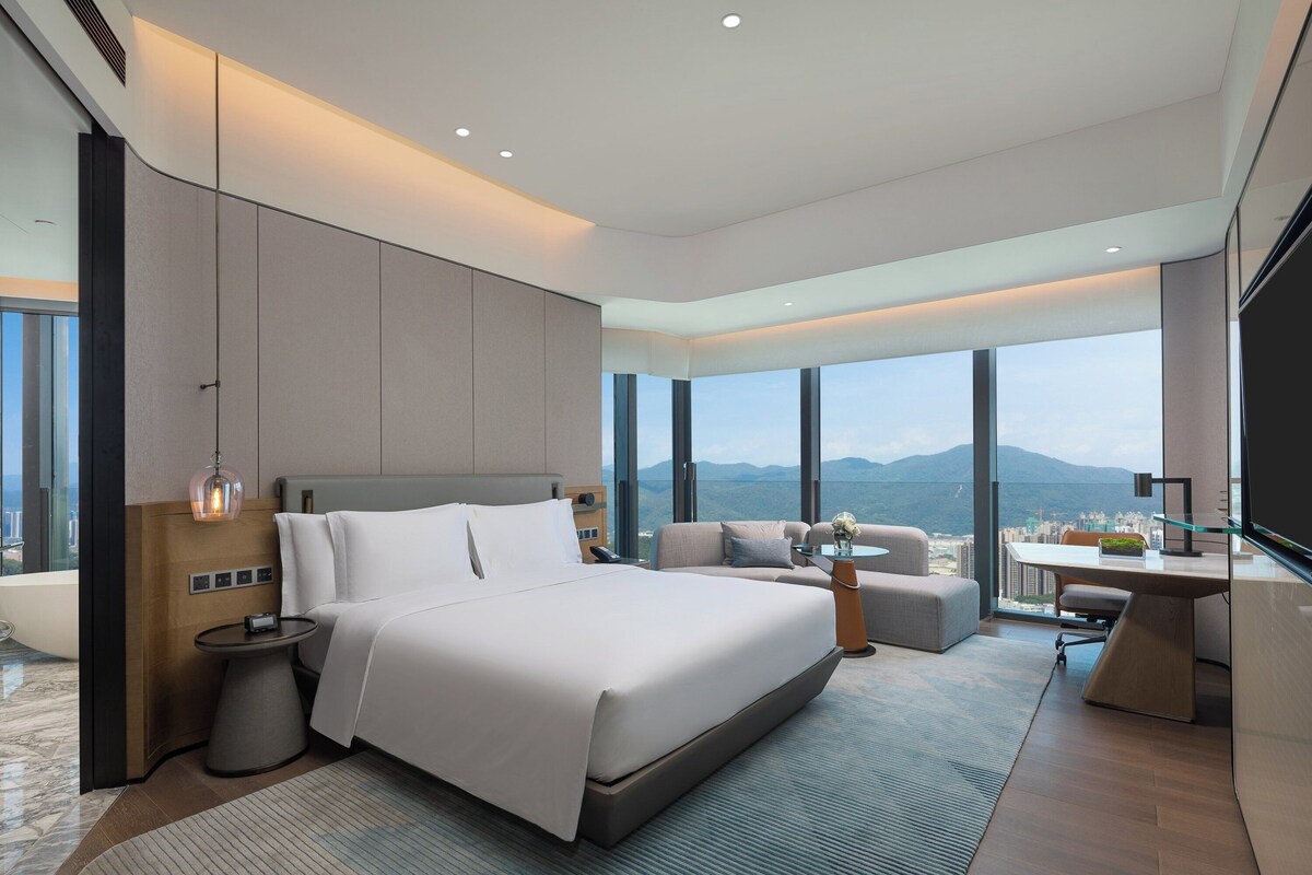 A modern hotel room with a large bed, a desk, and a view of the city.