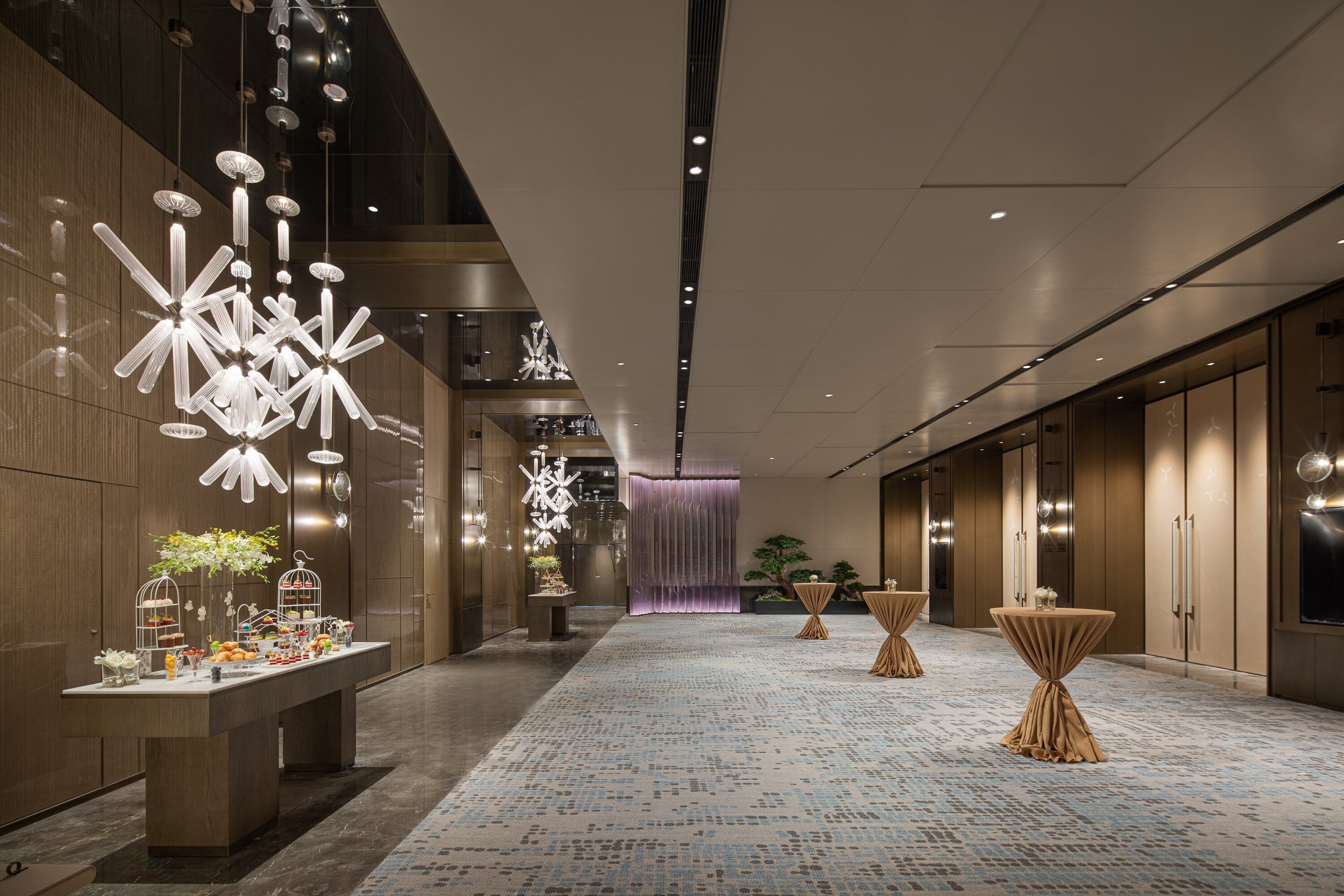 Un hall d’hôtel moderne avec un long comptoir d ’accueil, des luminaires décoratifs et une moquette à motifs.