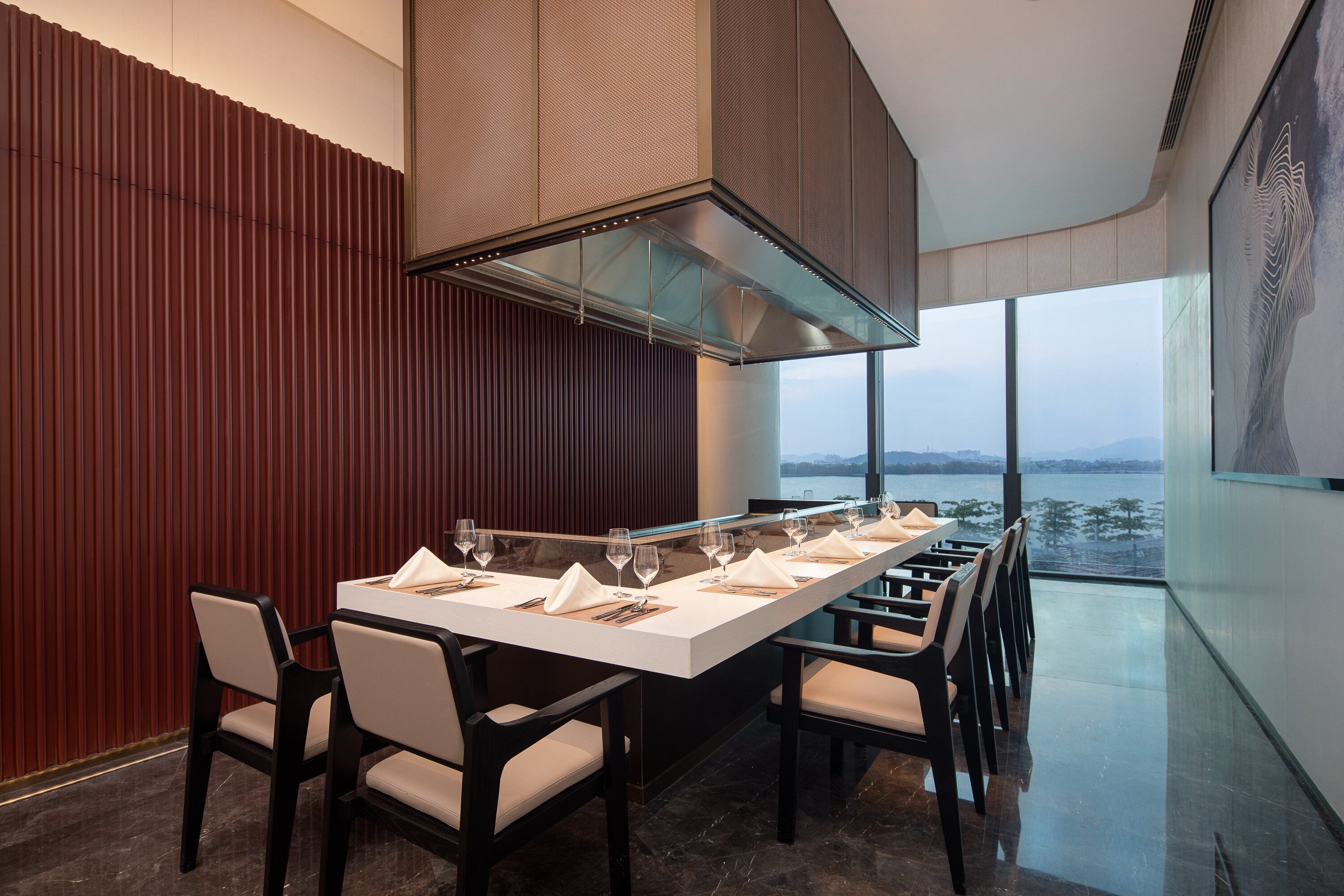 Uma sala de jantar moderna com uma mesa comprida posta para refeição, grandes janelas com vista para o exterior e mobiliário contemporâneo.