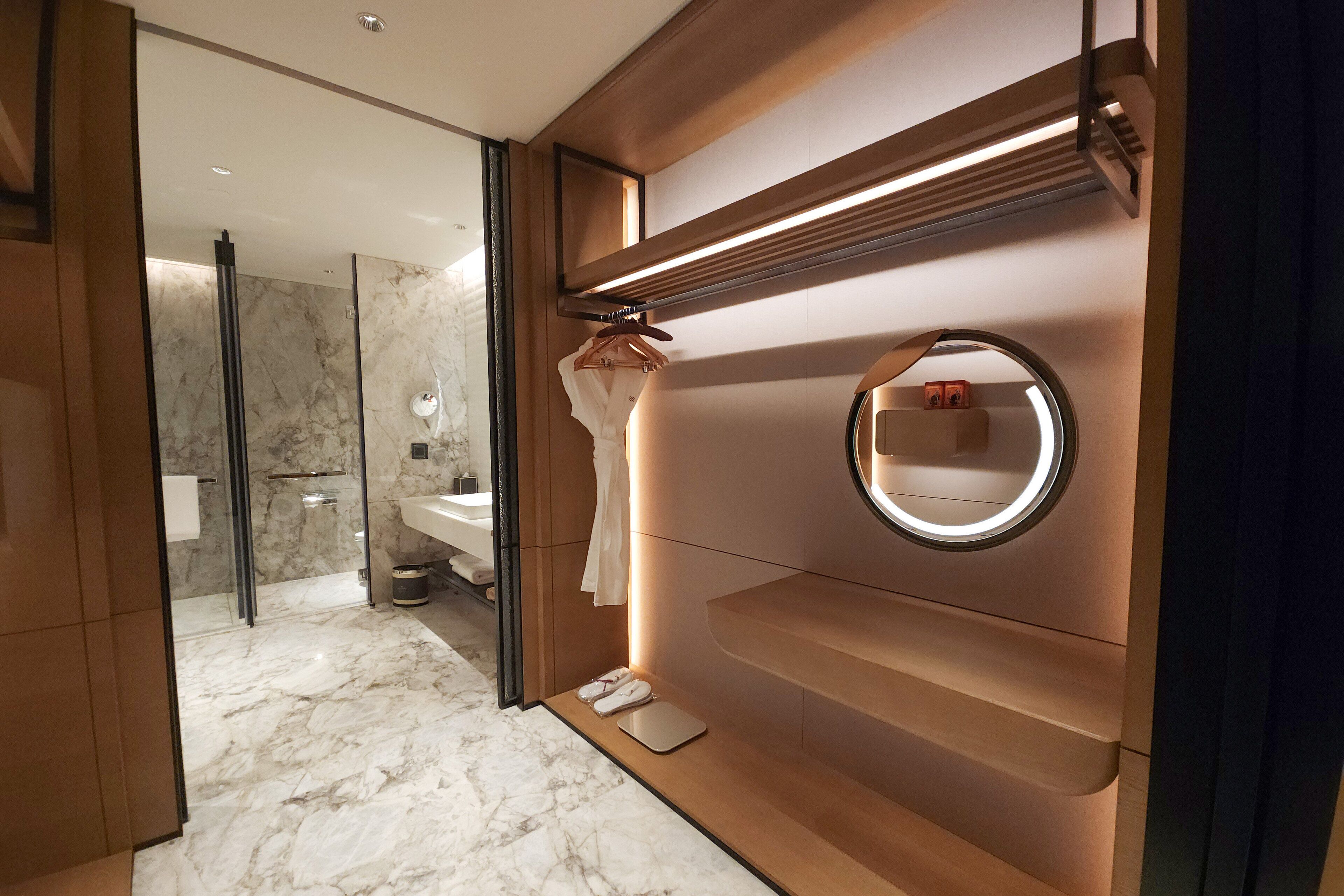 A modern bathroom with a marble floor, a round mirror, a towel rack, and a glass shower enclosure.