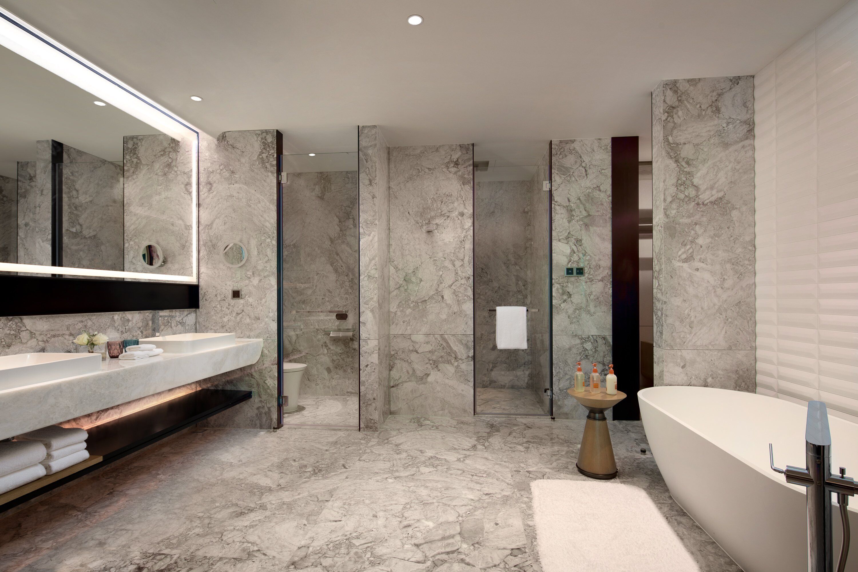 A modern bathroom with a marble floor, a large mirror, a bathtub, and a shower area.