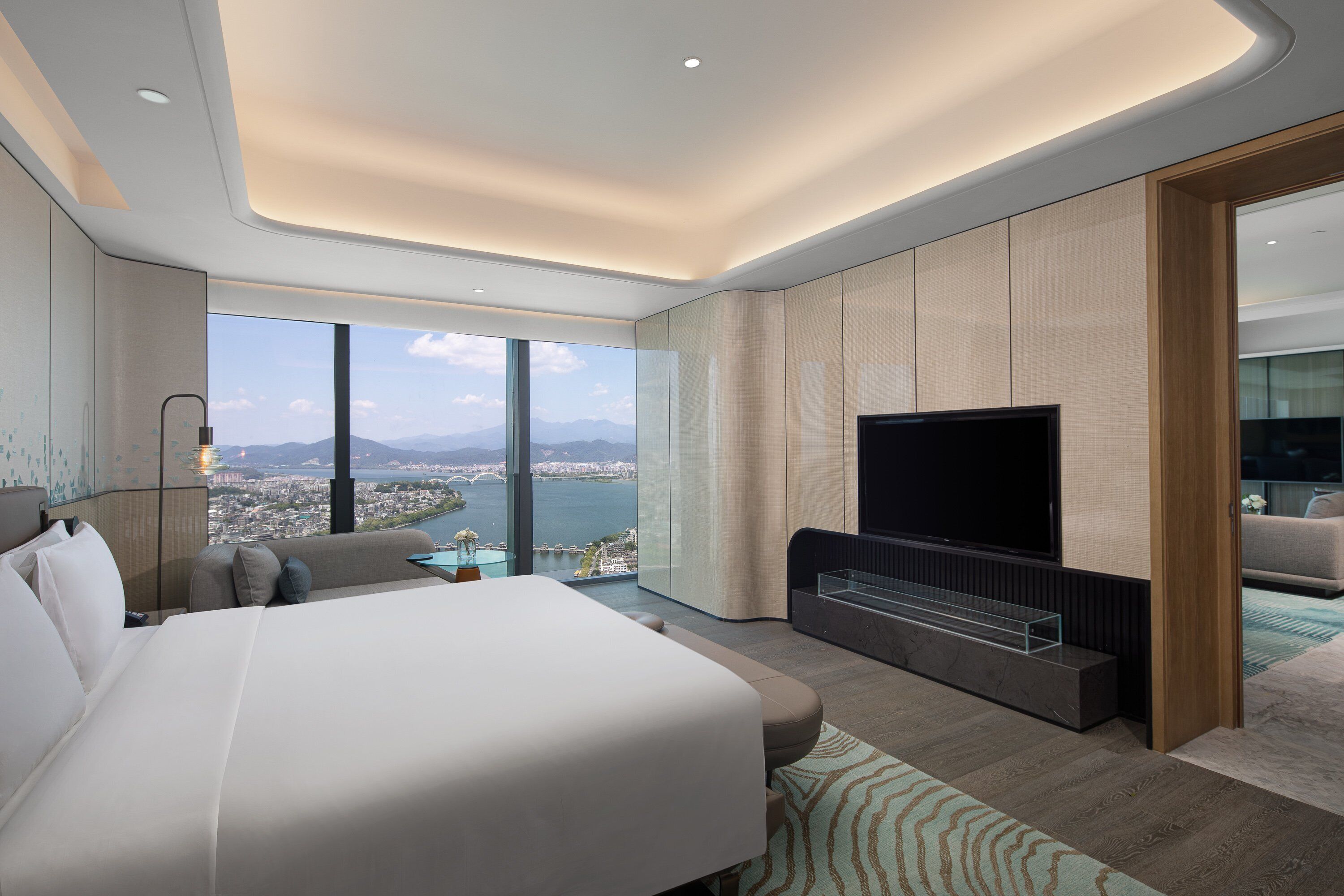 A modern hotel room with a large bed, a flat-screen TV, and a city view.