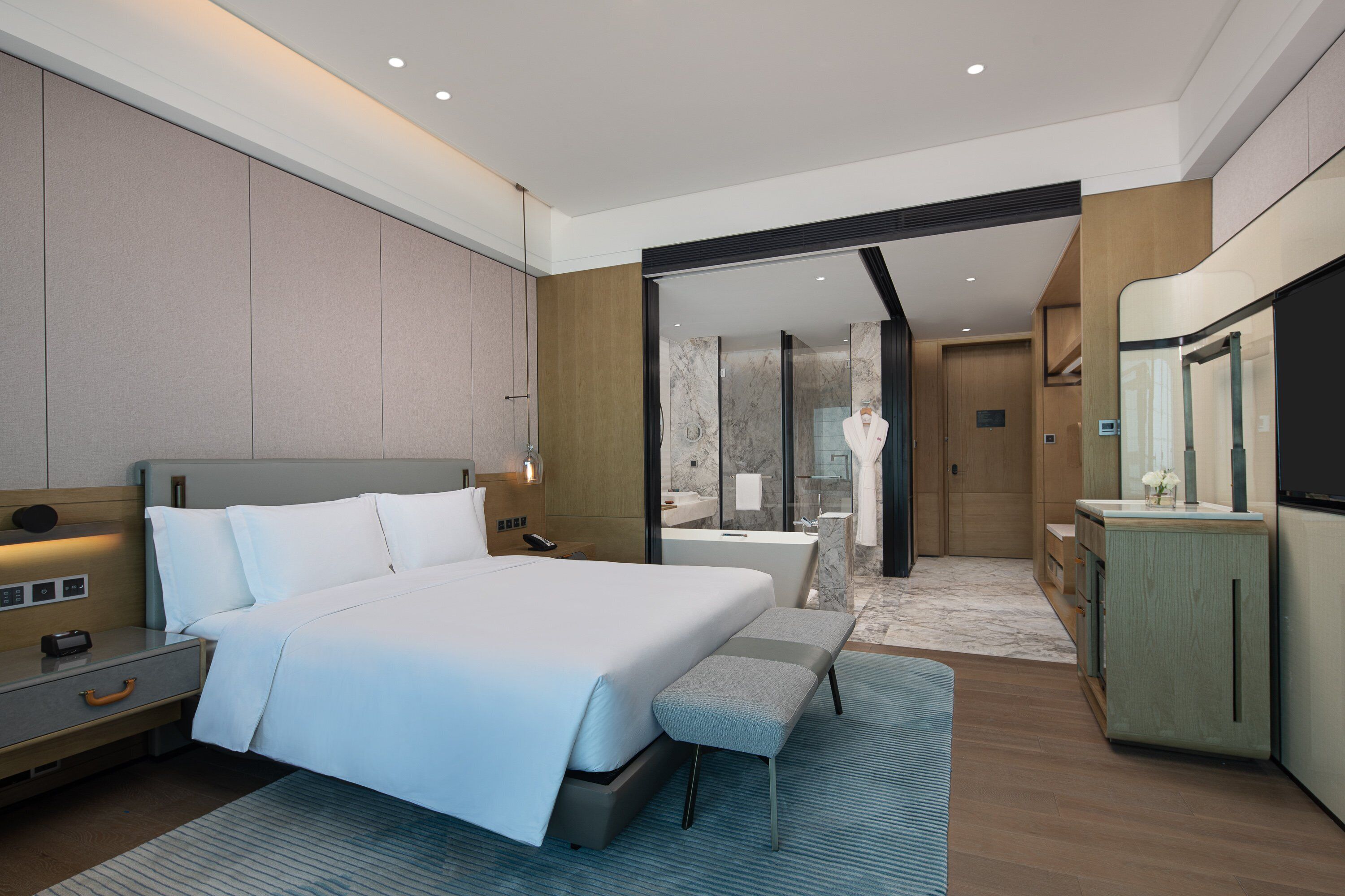 A modern hotel room with a large bed, bedside tables, a vanity with a mirror, and a shower area.