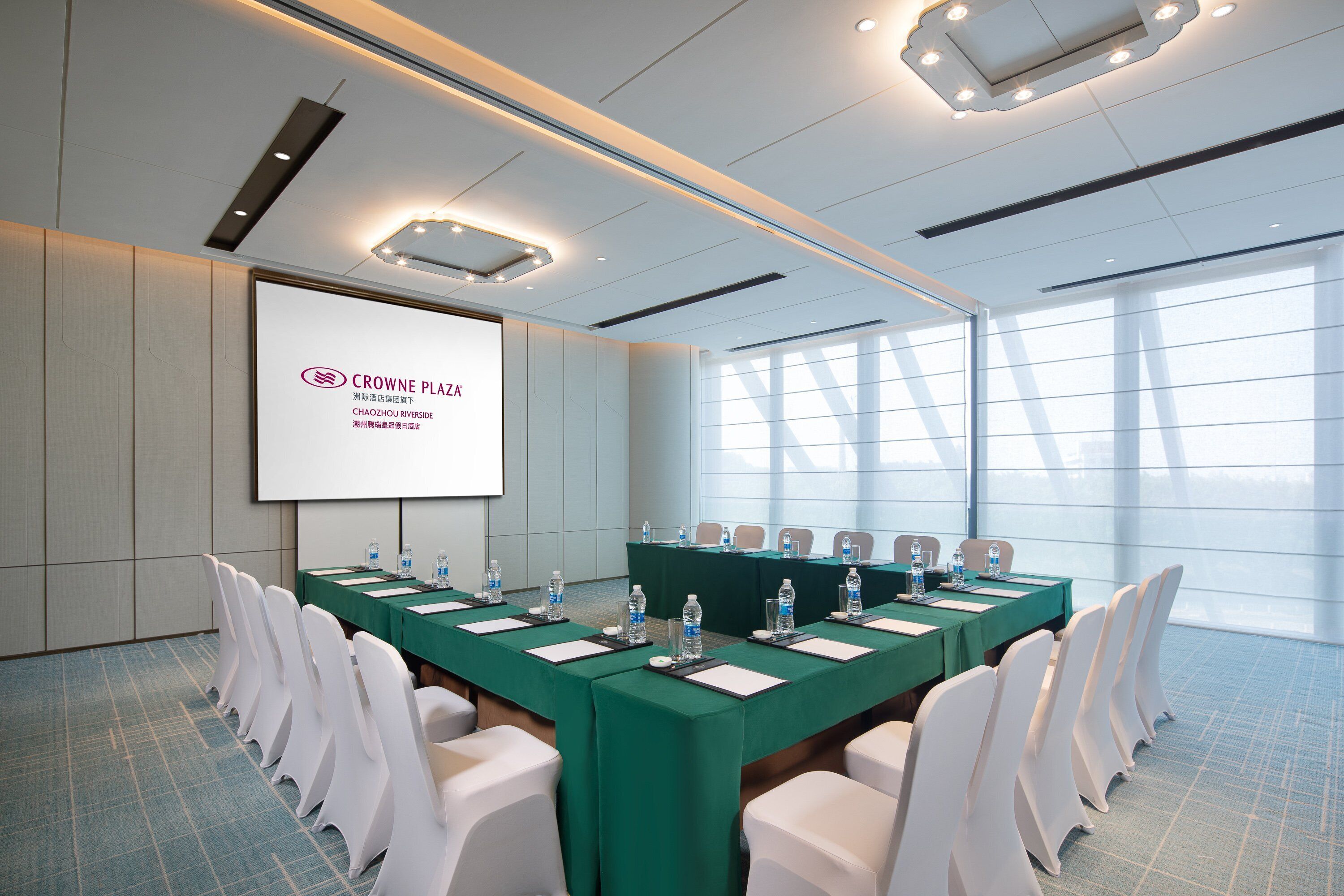 A conference room with a long table, white chairs, and a projector screen displaying text.