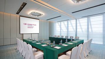 A conference room with a long table, white chairs, and a projector screen displaying text.