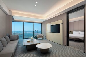 A modern hotel room with a large window offering a city view, a sofa, a coffee table, a TV, and a bed. - Crowne Plaza Chaozhou Riverside by IHG (Chaozhou)