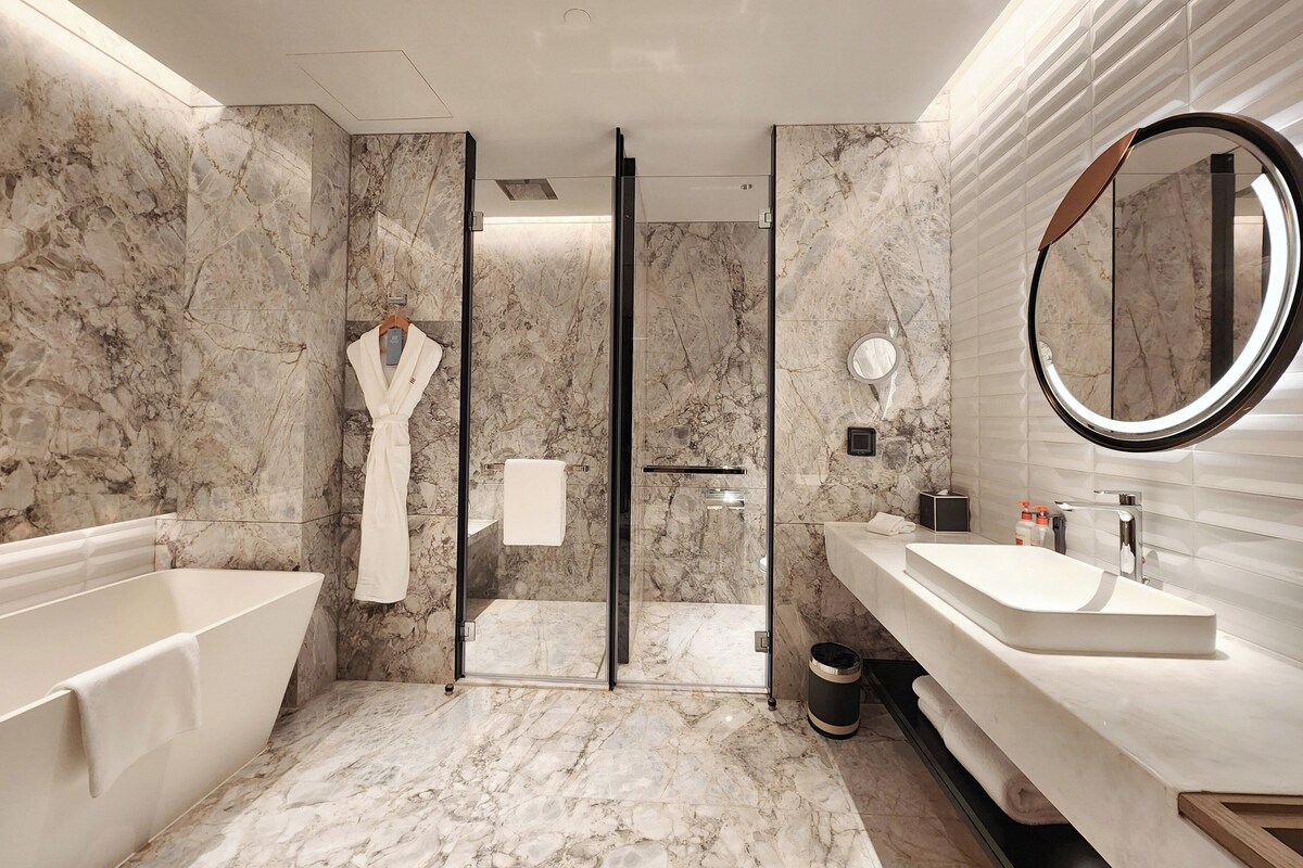 A modern bathroom with a marble floor, a freestanding bathtub, a large mirror, and a vanity with a sink.