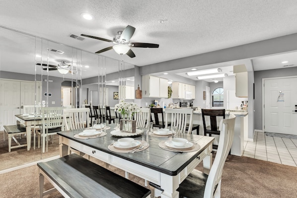 A modern kitchen with white cabinets, a dining area with a dark wooden table, and a ceiling fan.