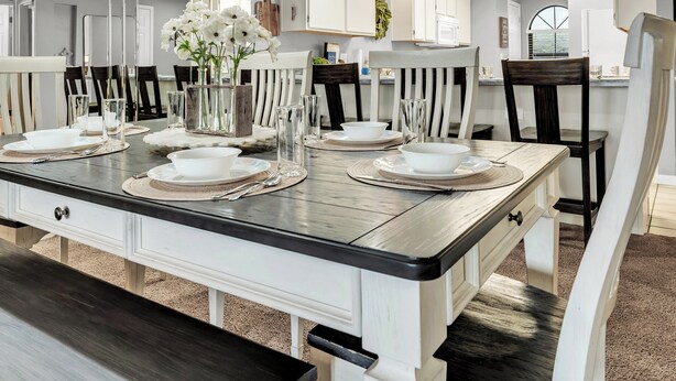 A dining area with a large table set for four, white chairs, a ceiling fan, and a kitchen in the background. - Fantastic Location! Indoor and Outdoor Pools, Hot tub, Golf & Shows! (Branson)