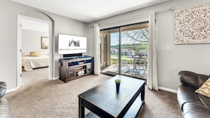 A modern living room with a TV, a coffee table, a sofa, and a sliding glass door leading to a patio. - Fantastic Location! Indoor and Outdoor Pools, Hot tub, Golf & Shows! (Branson)