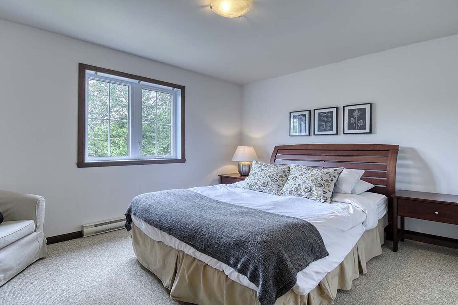 A bedroom with a large bed, a nightstand, a chair, and a window with a view of trees.