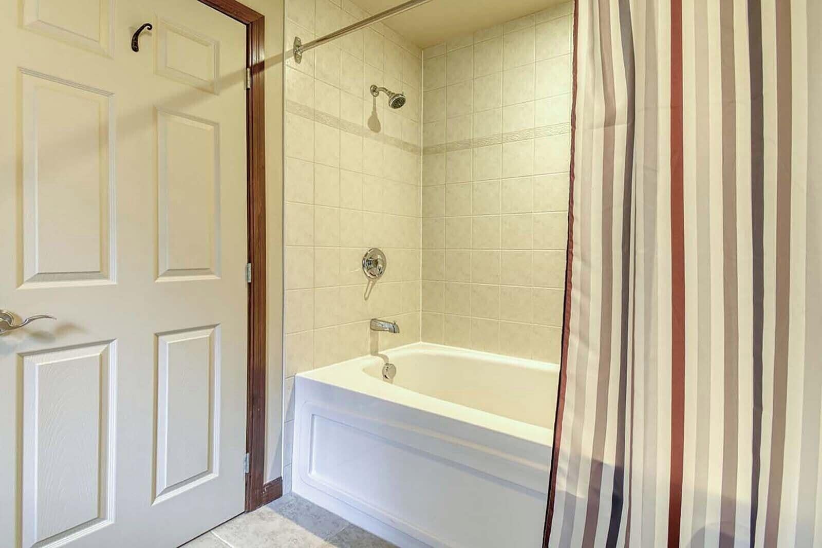 A bathroom with a white bathtub, a shower, and a door with a wooden frame.