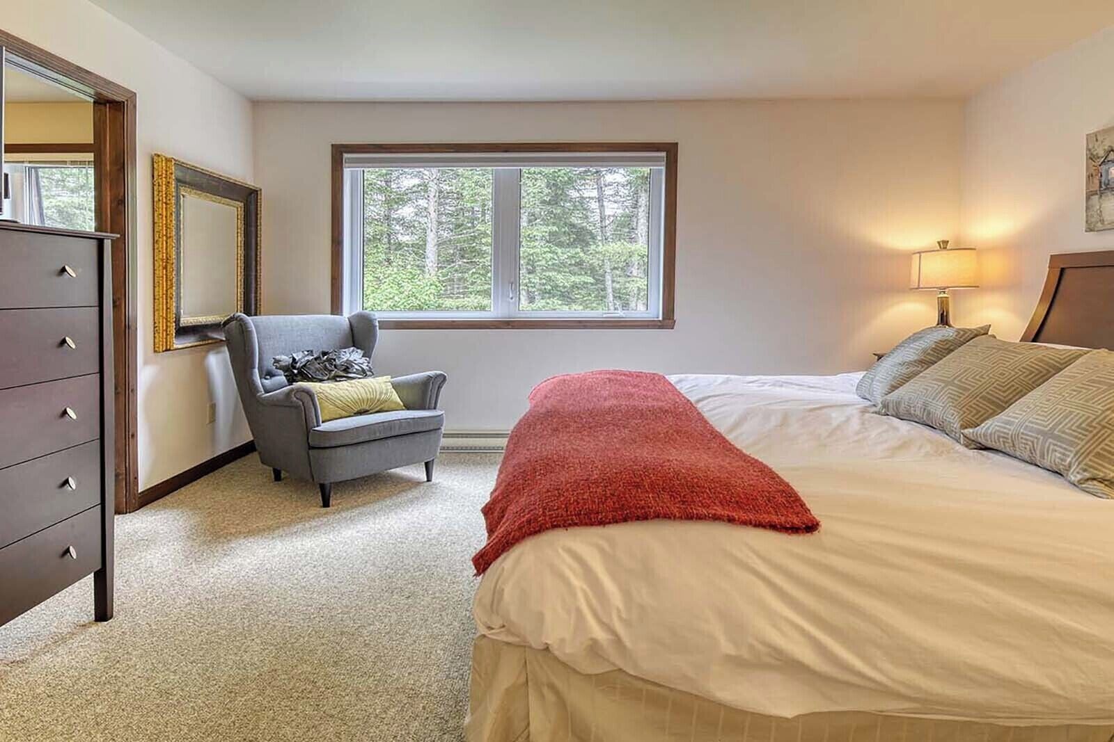 A bedroom with a bed, a dresser, a chair, a window, and a lamp.