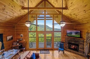Ein Holzblockhaus-Interieur mit Essbereich, Kamin und großem Fenster mit Blick auf eine Berglandschaft.