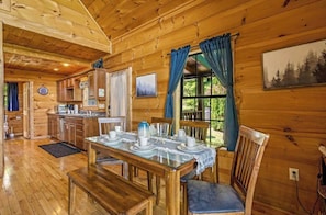 L’intérieur d’un chalet en bois comprend un coin repas, une cuisine et une grande fenêtre agrémentée de rideaux.