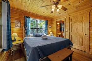 Een slaapkamer in chaletstijl met een bed, een bankje, een bureau en een raam met gordijnen.