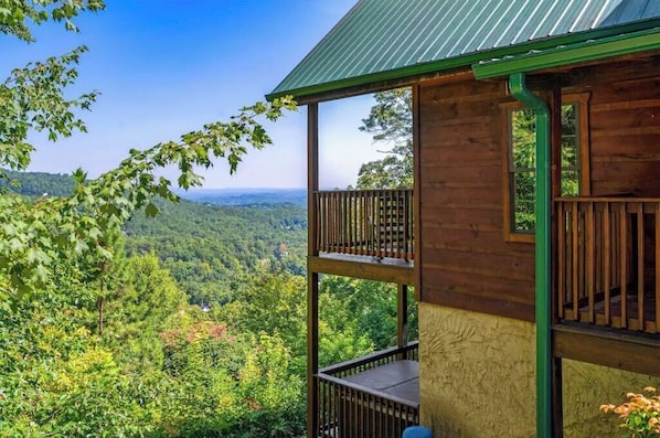 Een houten chalet met een balkon dat uitkijkt over een bebost dal.