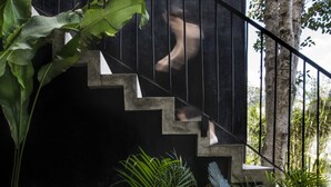 A staircase with a black railing leading to a dark wall, surrounded by lush green plants. - Villa LaGú • Luxury 5BR Jungle Villa • Pool, Spa & Chef (Tulum)