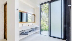 A modern bathroom with a large mirror, two sinks, and a sliding glass door leading to a balcony. - Villa LaGú • Luxury 5BR Jungle Villa • Pool, Spa & Chef (Tulum)