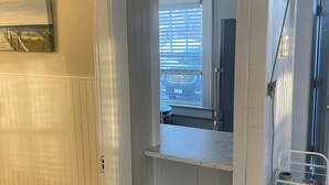 Una cucina con frigorifero integrato, uno sgabello in acciaio inossidabile e un piano di lavoro bianco.