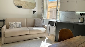 A compact living space with a sofa, a dining table, a kitchen area, and a window with a view of the outside. - Renovated apartment for 3 in the heart of old Antibes (Antibes)
