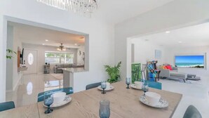 Un vaste espace de vie comprenant un coin repas avec une table pour quatre personnes, un grand téléviseur à écran plat et une vue sur l’océan.
