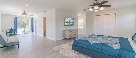 A bedroom with a large bed, a TV mounted on the wall, a ceiling fan, and a door leading to a balcony.