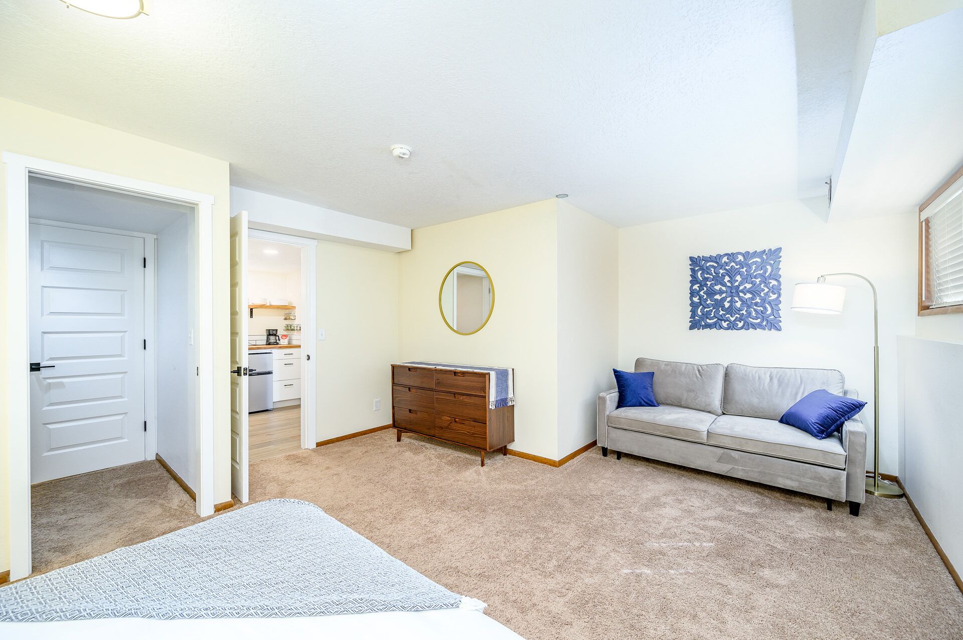 A bedroom with a bed, a dresser, a mirror, a sofa, and a lamp.