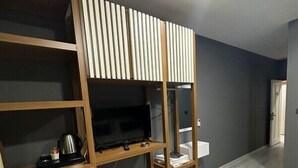 Une chambre moderne dotée d’une étagère intégrée pour la télévision, d’un petit coin cuisine et d’un mur gris.