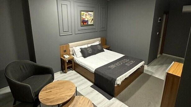 Une chambre à coucher moderne avec un grand lit, deux chaises, une petite table en bois et un tableau au mur.