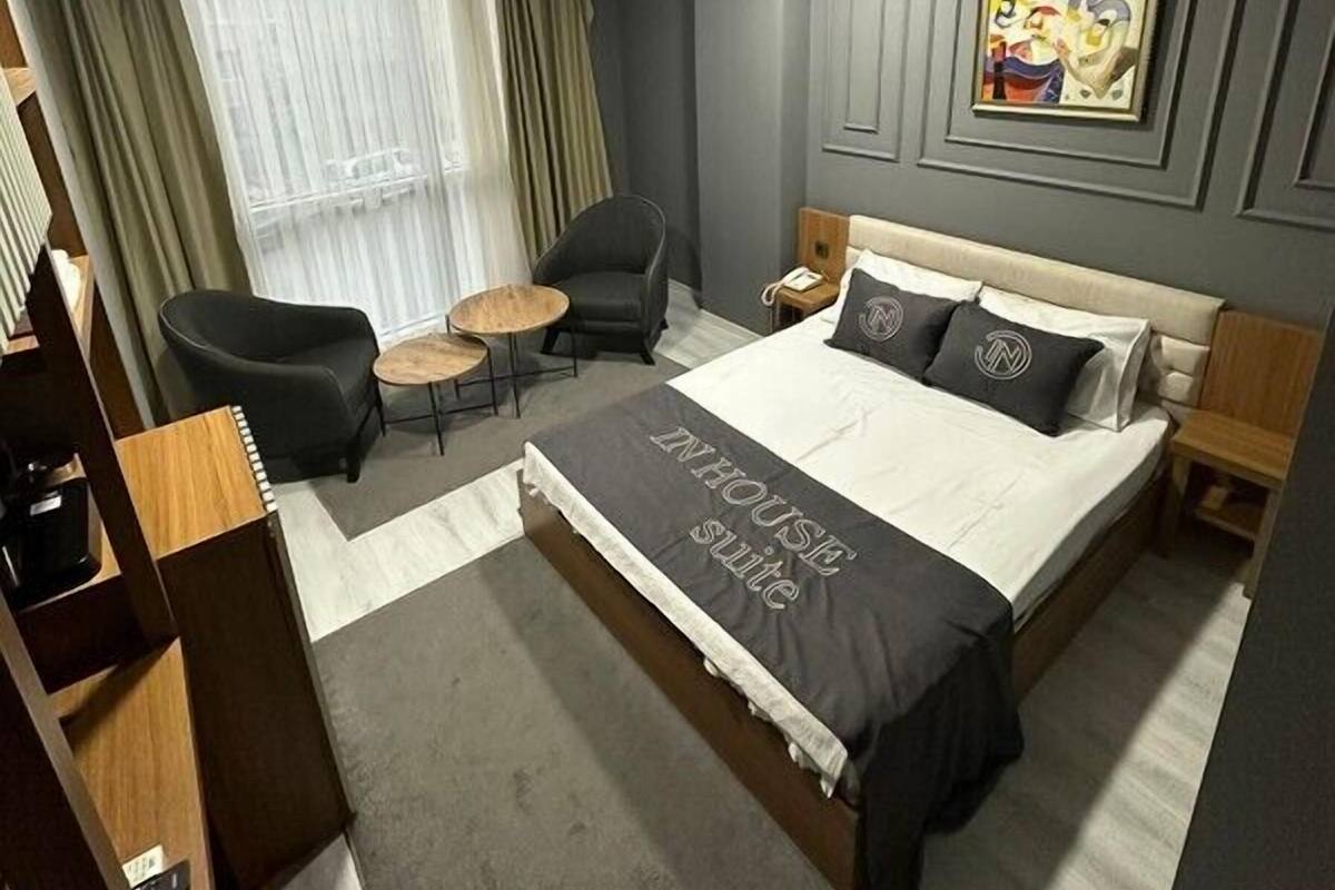 A hotel room with a large bed, a desk, a chair, a small table, and a window with curtains.
