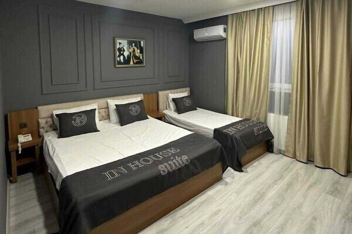 A hotel room with two beds, a painting on the wall, an air conditioning unit, and a window with curtains.