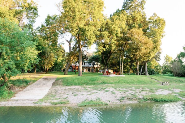 A park with a pathway leading to a house, surrounded by trees and a body of water.