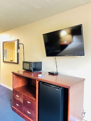 A hotel room with a wooden desk, a flat-screen TV, a microwave, a mini-fridge, a lamp, and a mirror. - Travelodge by Wyndham Canyonville (Canyonville)