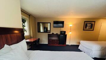 A hotel room with a large bed, a desk, a dresser, a television, and a lamp.