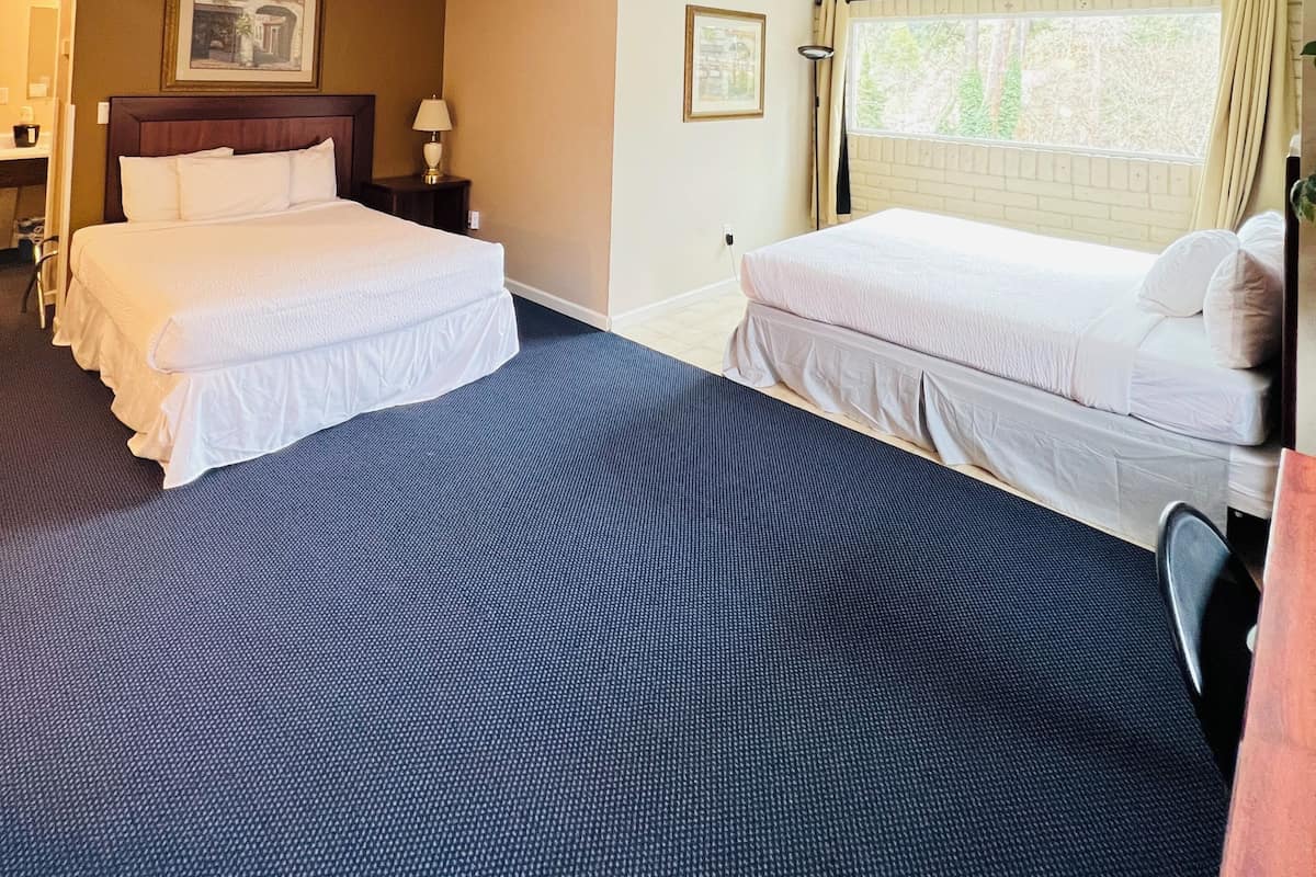 A hotel room with two beds, a desk, a chair, a window with curtains, and a picture on the wall.
