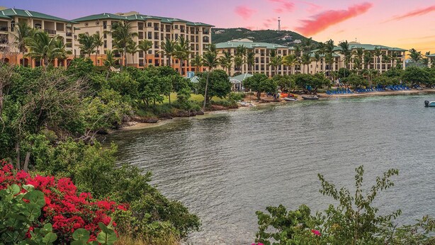 A hotel with multiple buildings, a beach, and palm trees.