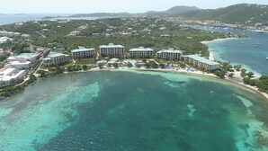 An aerial view of a coastal resort with multiple buildings, a beach, and clear turquoise waters.
