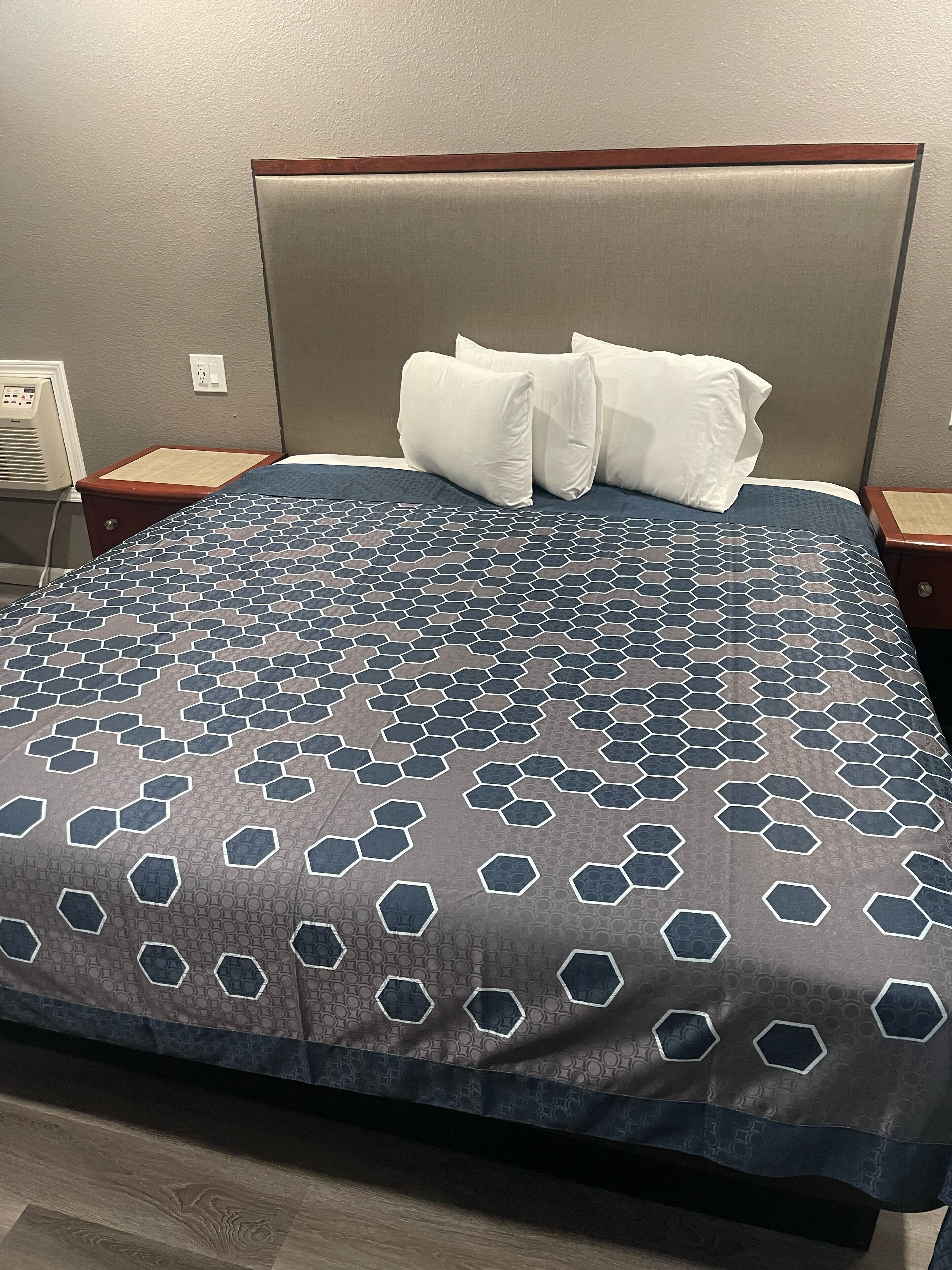 A hotel room with a bed featuring a geometric patterned bedspread, a wooden headboard, and two white pillows.